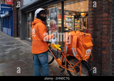 Ein Just Eat Delivery Person macht sich bereit, Greggs eingeben, um eine Bestellung für die Lieferung zu sammeln. Am frühen Sonntagmorgen in Lower Marsh, Waterloo London, aufgenommen Stockfoto