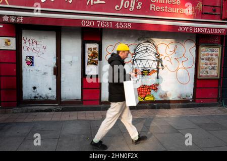 Ein Mann in gelber Farbe geht an einem geschlossenen chinesischen Restaurant in der New Oxford Street in London vorbei. Graffiti von Nathan Bowen. Stockfoto