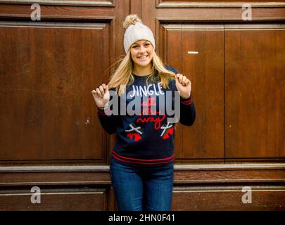 Ein blondes Mädchen in ihren Zwanzigern, das einen Weihnachtspullover und einen Hut trägt. Stockfoto