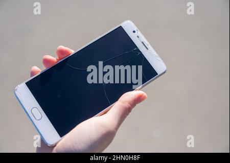 Frau hält Smartphone mit defekten Bildschirm im Freien. Stockfoto