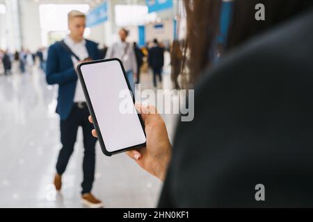 Blick auf ein Smartphone in weiblichen Händen mit leerem Bildschirm, mit Menschenmassen, Copyspace für Ihren individuellen Text. Stockfoto