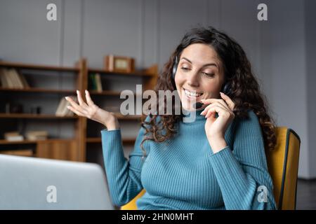 Junge, glückliche Frau, die ein Headset mit Freisprechfunktion trägt und den Kunden von zu Hause aus mit einem Mikrofon berät Stockfoto