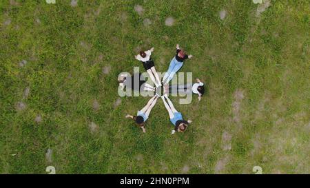 Freunde sitzen auf dem Gras, ihre Beine sind in einem Kreis zusammengefügt. Stockfoto