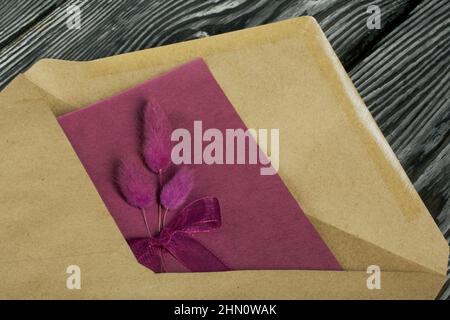 Grußkarte mit Statice-Zweigen und einem Umschlag. Auf Kiefernbrettern. Nahaufnahme. Stockfoto