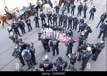 Dresden, Deutschland. 13th. Februar 2022. Polizeibeamte umgeben auf der Ostra-Allee Gegendemonstranten anlässlich einer Kundgebung von Neonazis. Die Prozession, die als schweigender marsch erklärt wurde, wurde von mehreren Gegendemonstrationen begleitet. Quelle: Sebastian Kahnert/dpa-Zentralbild/dpa/Alamy Live News Stockfoto