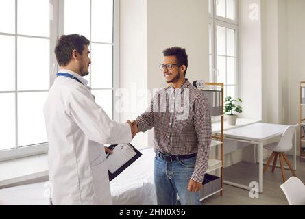 Freundlicher junger Arzt schüttelt die Hände und begrüßt den Patienten in einer modernen medizinischen Klinik. Stockfoto