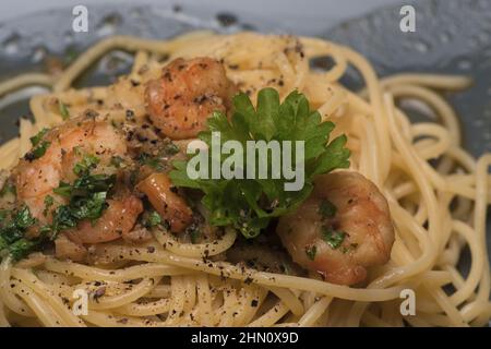 Extreme Nahaufnahme eines dunklen Tellers mit Garnelen auf köstlich dekorierten Alio olio Shrimp Pasta mit grüner Petersilie Stockfoto