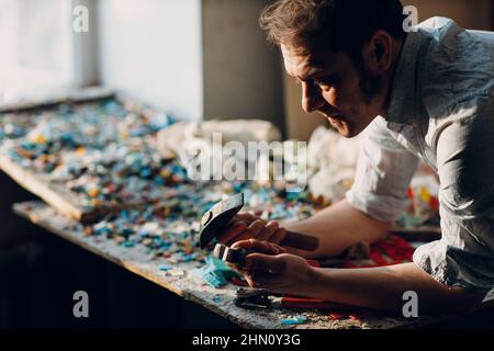 Handwerker männliche Meister Porträt halten Hammer und Smaltglas Stücke in Arm Hand für Mosaik-Kunstwerk in der Werkstatt. Stockfoto