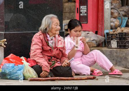 Ein junges Mädchen und eine Großmutter sitzen auf dem geschäftigen Lebensmittelmarkt in Cai Rang, in der Nähe von Can Tho, Mekong Delta, Südvietnam, unter Lebensmittelhändlern Stockfoto