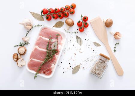 Rohes Fleisch und Holzspatel mit verschiedenen Gewürzen und Gemüse auf grauem Tischhintergrund, Draufsicht Stockfoto