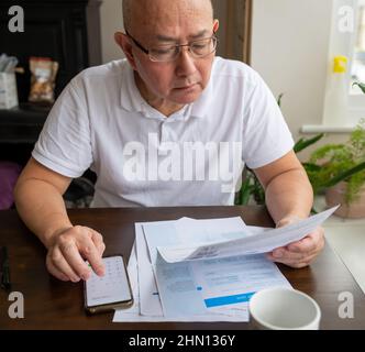 Ein älterer Mann, der an einem Tisch sitzt und die Anhebung der Kosten für Energie- und Steuerrechnungen berechnet. Konzept für Inflation und Lebenshaltungskosten. Stockfoto