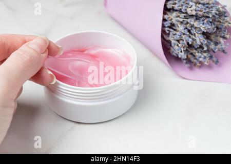 Weibliche Hände nehmen Augenflecken mit dem Löffel aus dem Behälter. Anti-Aging-Konzept. Augenpstches mit Lavendelextrakt. Schutz vor Einwickeln Stockfoto