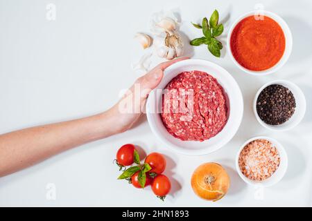 Rohes Hackfleisch, fertig für die Zubereitung von Fleischbällchen. Dekoriert mit Zutaten wie Zwiebeln, Basilikum, Tomatensauce, Pfeffer und Salz. Stockfoto