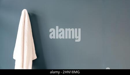 Weißes Badetuch, das an einem Haken hängt, blauer Wandhintergrund im Badezimmer. Leerer Raum, Vorlage. Stockfoto