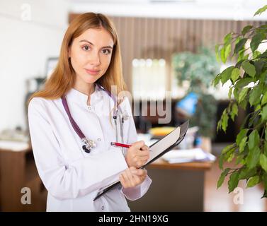 Die junge Therapeutin schreibt Notizen auf eine Tablette und steht in einem Büro Stockfoto