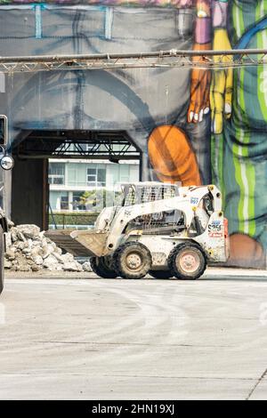 Minibagger-Planierraupe vor bemalten Wandmalereien auf Zementsilos auf Granville Island Vancouver British Columbia kanada Stockfoto