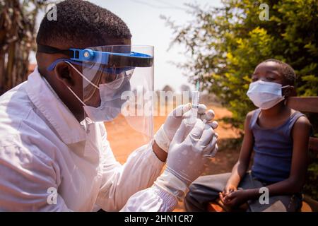 Der Arzt passt die Spritze an, um einem afrikanischen Kind den Impfstoff zu injizieren. Konzept der Covid-19-Impfung in Afrika. Coronavirus-Impfstoff. Stockfoto