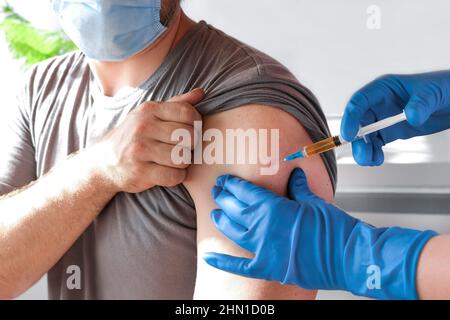 Hände eines Arztes, der Coronavirus-Covid-19-Impfstoff in eine Impfspritze in den Armmuskel des kaukasischen Mannes zur Covid-Immunisierung injiziert. Stockfoto