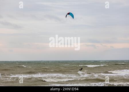 East Preston, Großbritannien, 13th. Februar 2022. Windsurfer, die bei starken Winden am East Preston Beach in West Sussex zum Wasser fahren. Quelle: Steven Paston/Alamy Live News Stockfoto