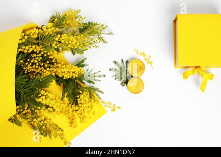 Zweige gelber Mimosenblüten, französische gelbe Makronen in Form von 8 und gelbe Geschenkbox mit Schleife. Gruß zum Internationalen Frauentag Stockfoto