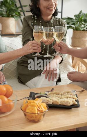 Beschnittenes Bild von älteren Frauen, die Gläser mit Champagner und leckerem Essen zu Hause anklimmten Stockfoto