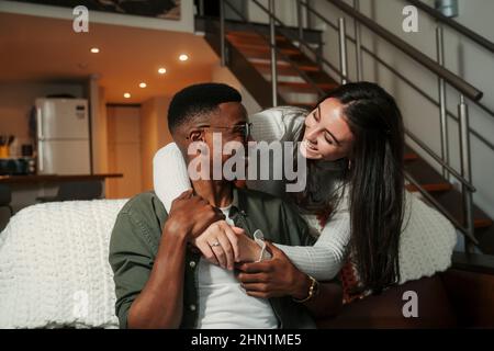 Afroamerikanischer Mann, der auf dem Sofa sitzt und sich mit einer kaukasischen Frau umarmt Stockfoto