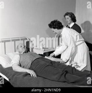 1950s, historisch, ein männlicher Stahlarbeiter, der auf einem Metallbett liegt und einen Bluttest von einer Krankenschwester in der Fabrik, Wales, England, Großbritannien, durchgeführt hat. Stockfoto