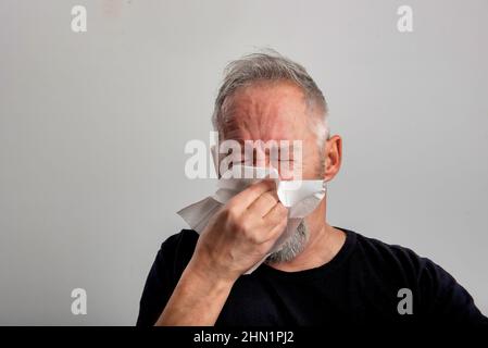 Kranker grauhaariger Mann mittleren Alters niest und bläst seine Nase Stockfoto