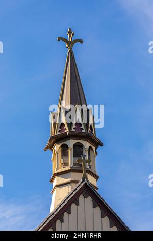 Eine Spitze einer kleinen Kirche mit Kreuz in der Landschaft. Details eines Kirchteigs einer Holzkirche in blauem Himmel im Hintergrund Stockfoto