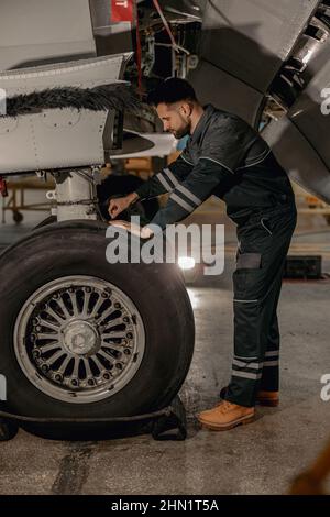 Männlicher Mechaniker repariert Flugzeugrad in Hangar Stockfoto