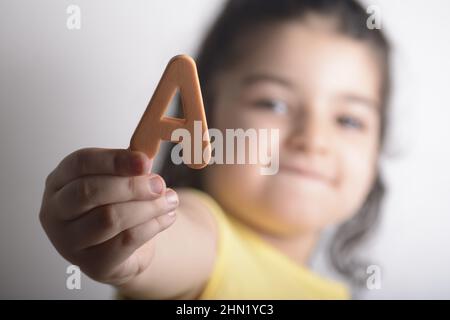 Kleines Mädchen mit Einem schwammigen Buchstaben in der rechten Hand Stockfoto