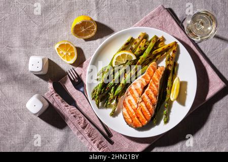Gegrilltes Lachssteak mit gebratenem Spargel und Zitrone auf einem Teller auf einer Leinentischdecke Stockfoto