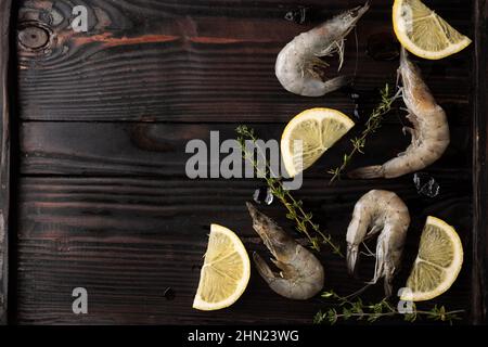 Garnelen, Garnelen mit Zitrone, Eiswürfeln und Thymian auf Holzgrund, gefrorene Meeresfrüchte. Stockfoto