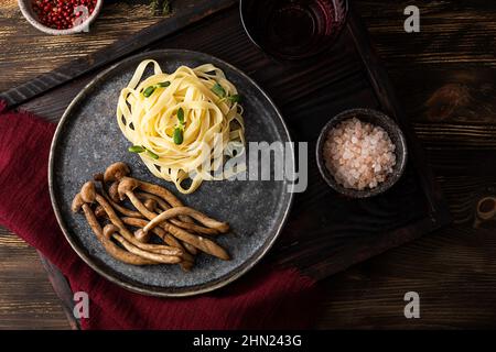 Teller mit gebratenen Pilzen und Pasta, gekochten Shimeji und Nudeln auf Holzboden. Stockfoto