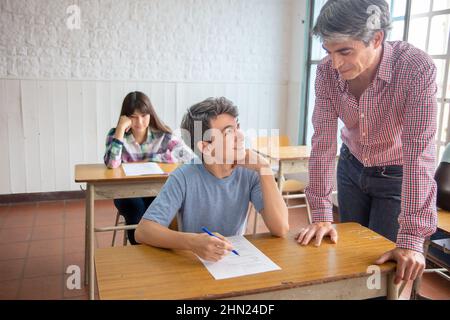 Gruppe von multiethnischen Gymnasiasten mit Test im Klassenzimmer, Lehrer beaufsichtigt Stockfoto