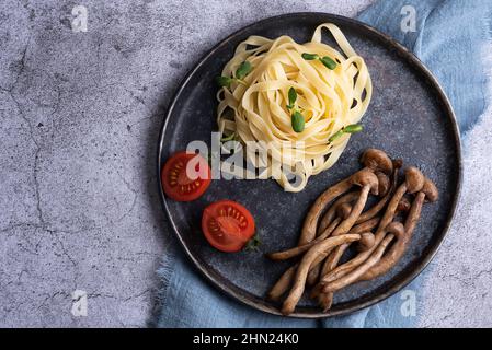 Gebratene Shimeji serviert mit Nudeln auf dem Teller, Pilze und Pasta auf grauem Hintergrund. Stockfoto