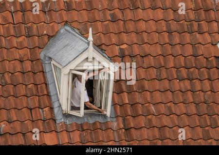 Neues Fenster wird in ein Dorma-Dachfenster in Whitby eingebaut. Mann, der das Fenster hält, das von Dachziegeln umgeben ist. Stockfoto