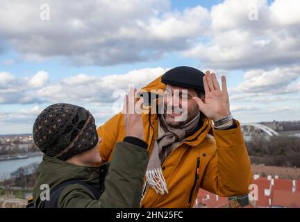 Lächelnder Vater und sein kleiner Sohn geben sich High-Five, während er im kalten Winter in Jacken im Freien steht. Stockfoto