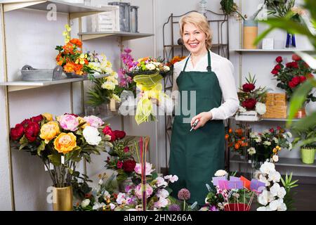 Weibliche Floristin trägt eine Schürze und bereitet gerne Blumen vor Stockfoto