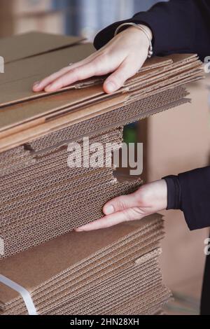 Frau nimmt gefaltete Stapel von Wellpappe zum Verpacken im Lager, Stapel von Wellpappenblättern und gebrauchsfertig Stockfoto