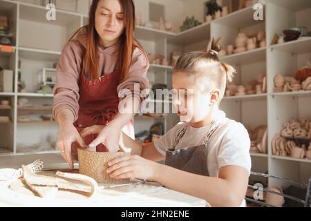 Professioneller Töpfer, der jungen Jungen bei der Herstellung von Teetassen beim Keramikkurs hilft Stockfoto