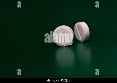 Zwei runde weiße Pillen auf grünem Hintergrund stehen auf ihrer Seite. Medizinisches Thema. Selektiver Fokus. Seitenansicht. Stockfoto