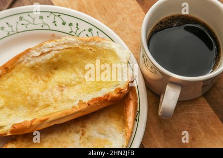 Goiânia, Goias, Brasilien – 13. Februar 2022: Zwei Brötchen auf dem Teller und eine Tasse Kaffee auf einer Holzoberfläche. Stockfoto