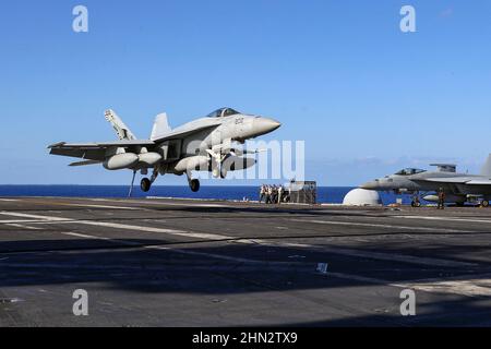 PHILIPPINISCHES MEER (Feb 13, 2022) ein F/A-18E Super Hornet, der den „Tophoattern“ des Strike Fighter Squadron (VFA) 14 mit dem Flugzeugträger USS Abraham Lincoln (CVN 72) der Nimitz-Klasse zugewiesen wurde, bereitet sich darauf vor, während des Flugbetriebs eine verhaftete Landung auf dem Flugdeck zu machen, um die Jungle Warfare Exercise 22 (JWX 22) über Okinawa zu unterstützen, Japan, 13. Februar 2022. JWX 22 ist eine groß angelegte Schulung vor Ort, die sich auf die Nutzung der integrierten Fähigkeiten gemeinsamer und verwandter Partner konzentriert, um das Bewusstsein, die Manöver und die Brände in einer verteilten maritimen Umgebung zu stärken. (USA Navy Pho Stockfoto