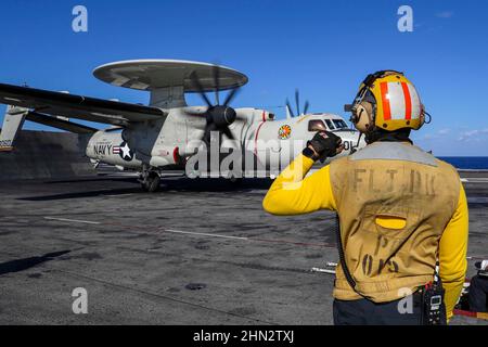 PHILIPPINISCHES MEER (Feb 13, 2022) die US Navy Aviation Boatswain’s Mate (Handling) 1st Class Doran Branch, aus Fairfield, Kalifornien, mit dem Flugzeugträger USS Abraham Lincoln (CVN 72) der Nimitz-Klasse, leitet einen E-2D Hawkeye, der den „Wallbangers“ der Carrier Airborne Early Warning Squadron (VAW) 117 zugewiesen wurde, Während des Flugbetriebs zur Unterstützung der Jungle Warfare Exercise 22 (JWX 22) in Okinawa, Japan, 13. Februar 2022. JWX 22 ist eine umfassende Schulung vor Ort, bei der die integrierten Fähigkeiten gemeinsamer und verwandter Partner genutzt werden, um das Bewusstsein, die Manöver und die Brandbekämpfung in allen Bereichen zu stärken Stockfoto