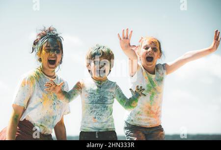 Lustige Kinder Gesicht in Farbe Splash, farbige Pulver auf Kinder Körper. Fröhliche Freunde zeigen Hände in hellen Farben gemalt. Bunte, schmutzige Leute. Stockfoto