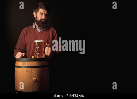 Fröhlicher Brauer. Emotionaler lustiger bärtiger betrunkener Hipster hält Craft-Flaschenbier. Fröhlicher Brauer, der Glas mit Bier hält. Glücklicher lächelnder Mann mit Bier. Stockfoto