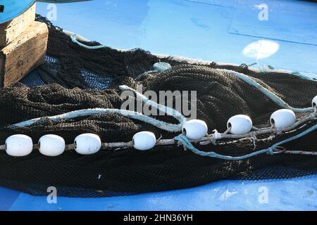 Kleine weiße Bojen auf schwarzem Fischernetz vor blauem Hintergrund. Stockfoto