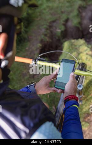 Nicht erkennbarer männlicher Mountainbiker von hinten, der eine Karte auf einer gps-App auf seinem Smartphone abcheckt Stockfoto