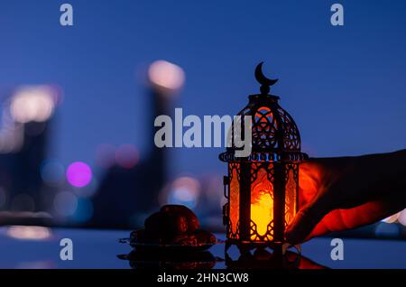Selektiver Fokus der Laterne, die Mond-Symbol auf der Oberseite und kleine Teller mit Daten Frucht mit Stadthintergrund für das muslimische Fest des heiligen Monats haben Stockfoto